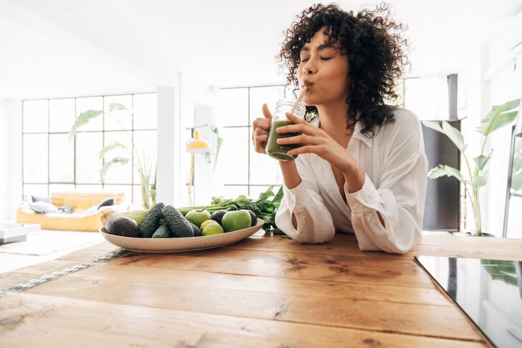 Woman enjoying a green smoothie indoors.